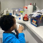 A young boy watches a cartoon on a cell phone in a kitchen.