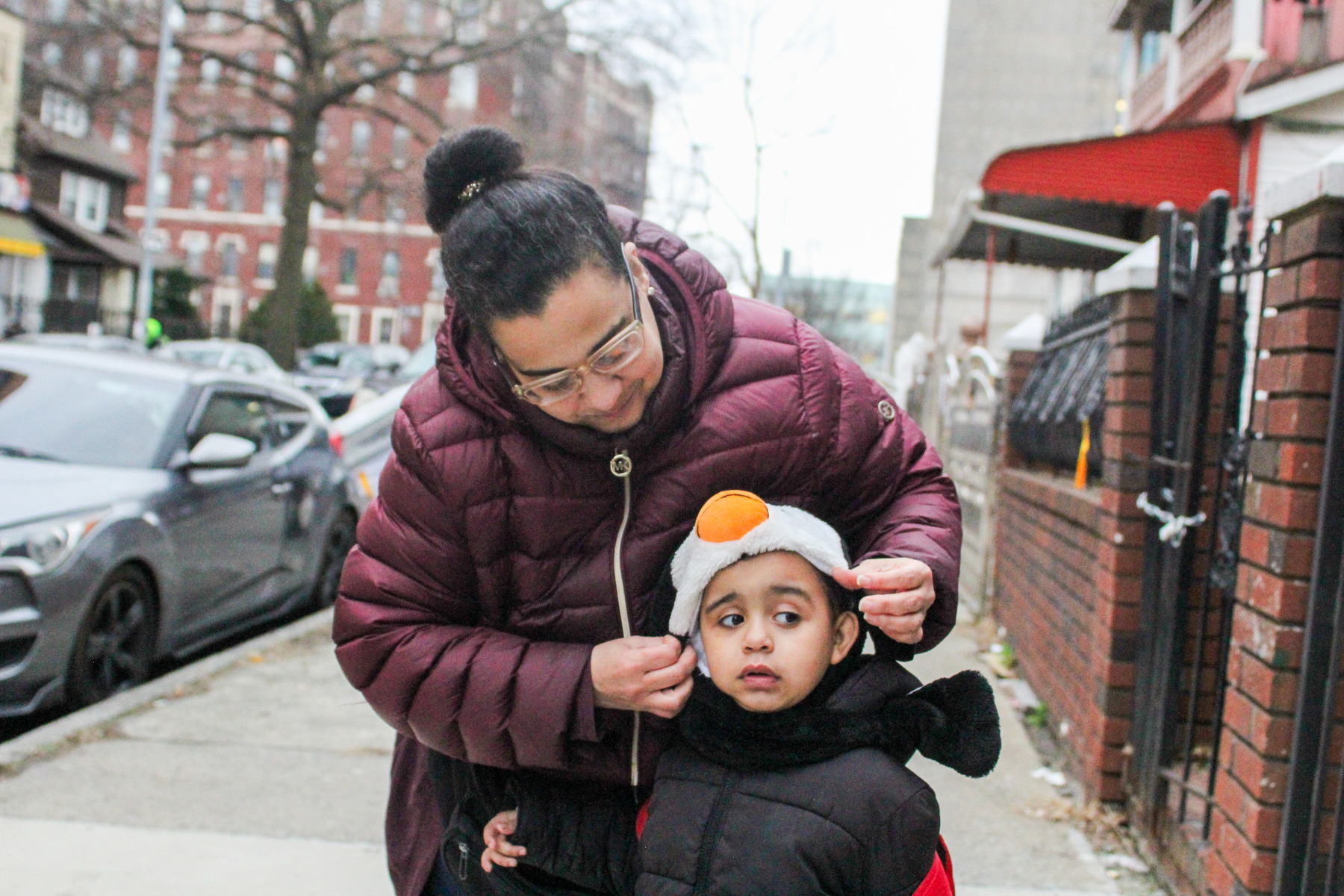 A woman places a hat on a child's head, while standing on a sidewalk