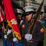 A line of Marines carry flags and guns in a parade.