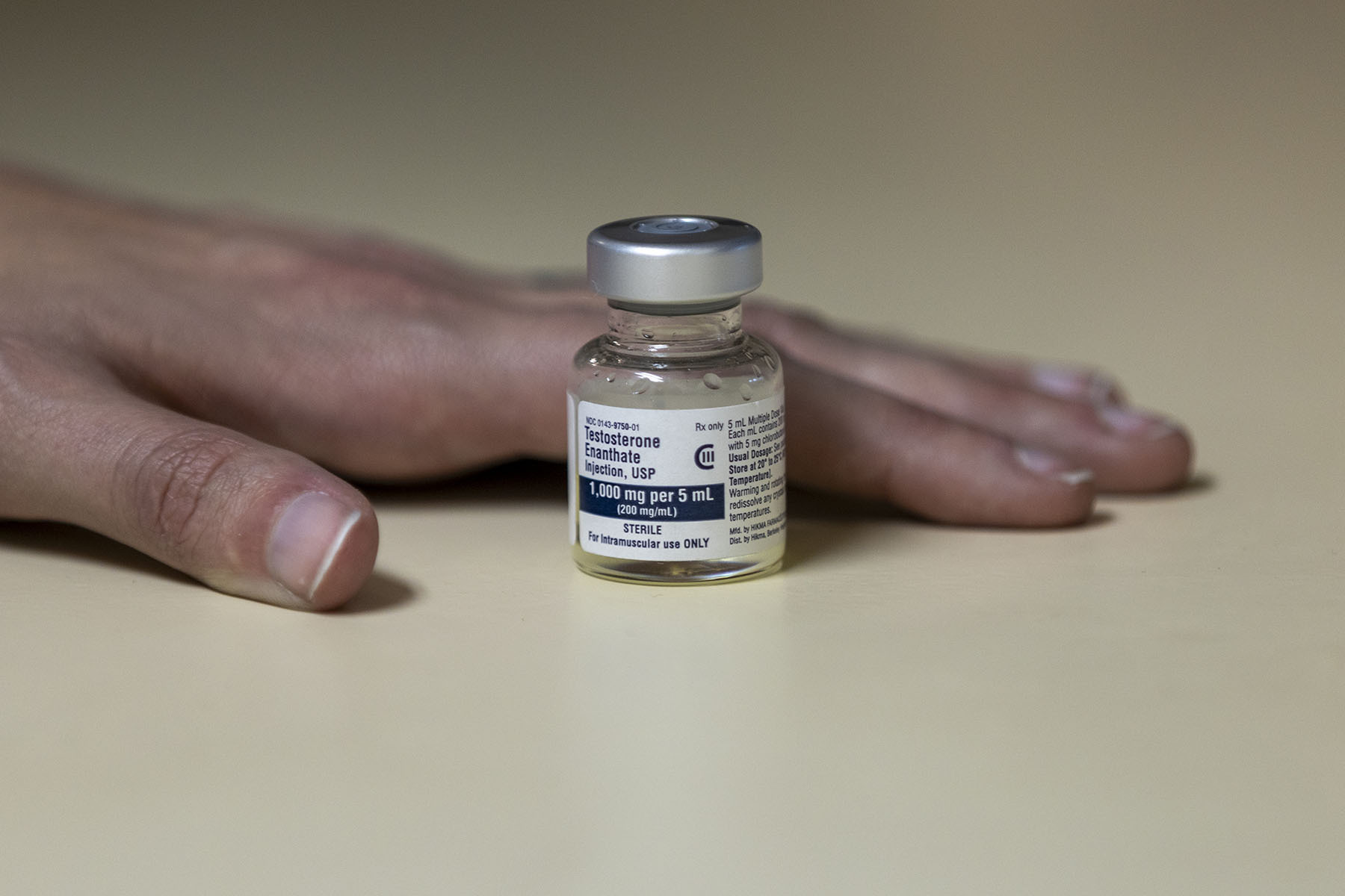 A hand lays beside a vial of testosterone.