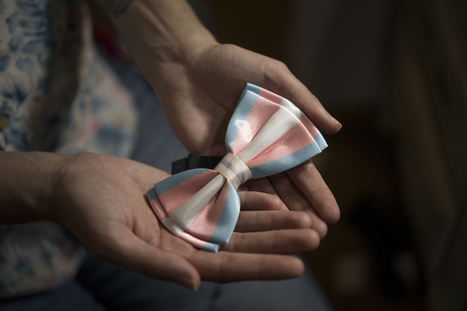 A bow tie in the colors of the trans pride flag are held in two open palms.