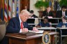 President Donald Trump signs an executive order surrounded by children at school desks also signing fake executive orders in the East Room of the White house.