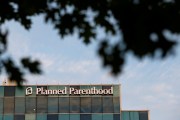 A Planned Parenthood building against a blue sky framed by shadows from tree leaves.