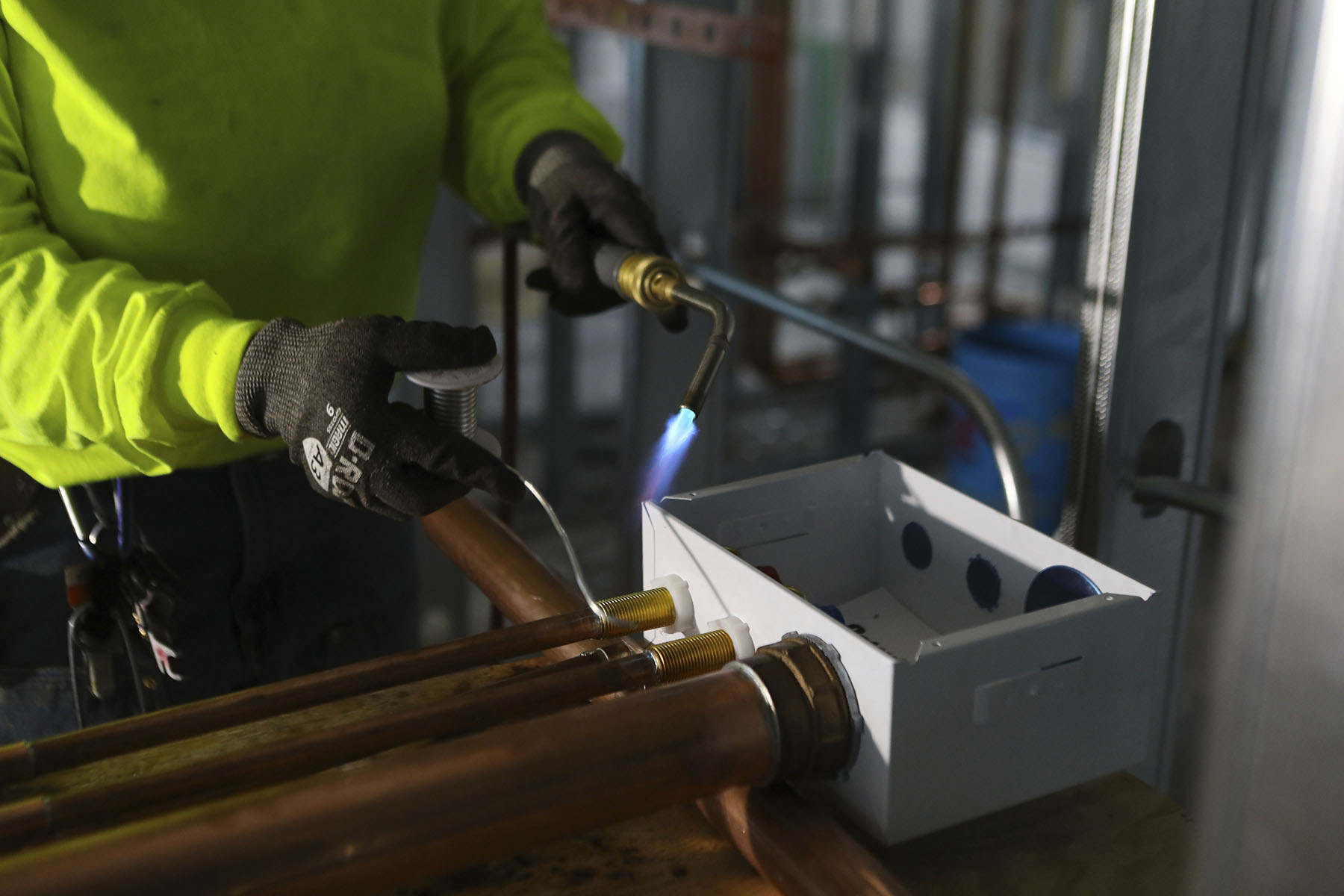 A plumbing apprentice welds pipes at a high rise residence under construction.