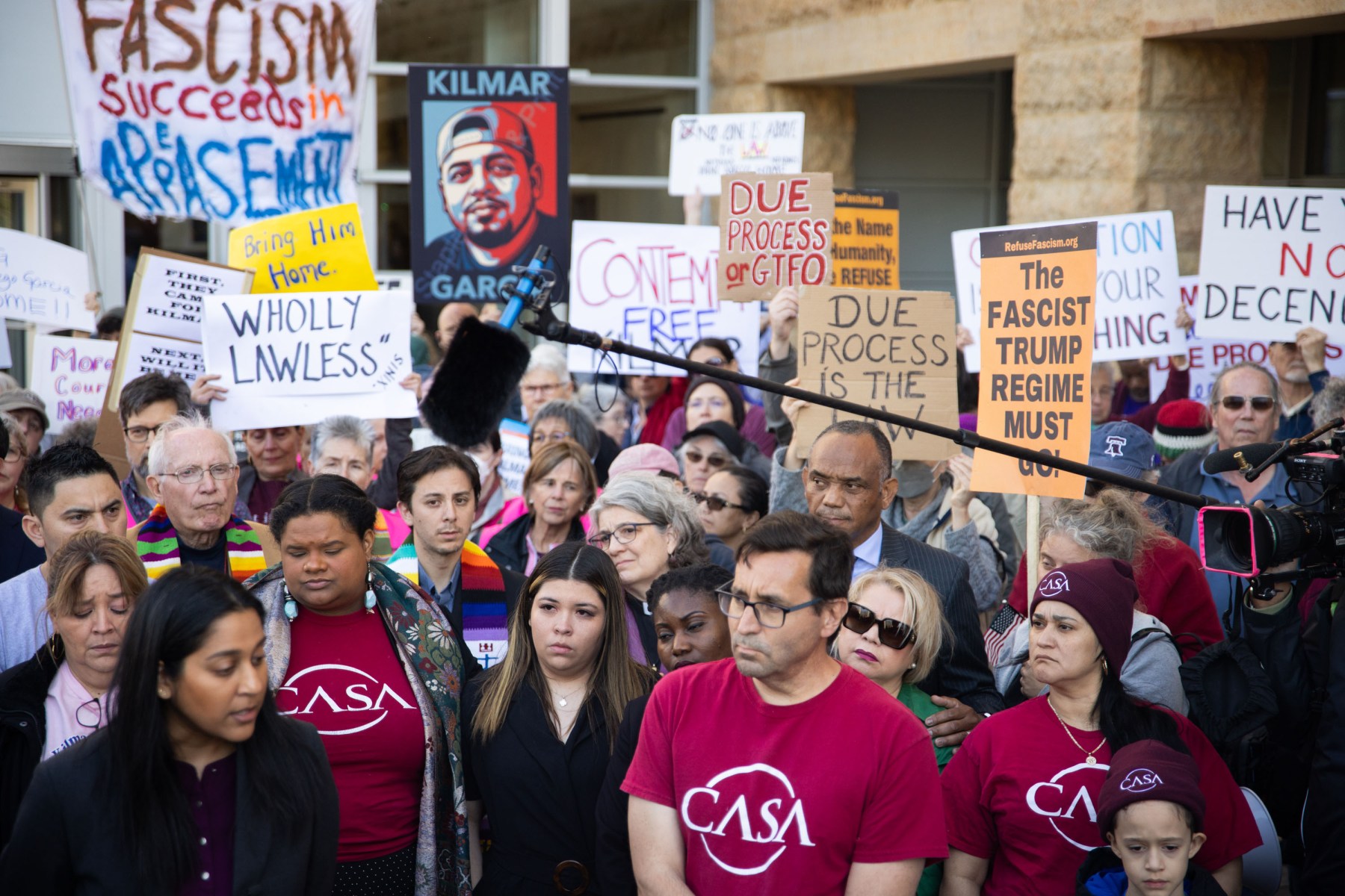 A large crowd gathers outside a courthouse holding protest signs demanding due process and justice for Kilmar Abrego García. Jennifer Vasquez Sura stands near the front.