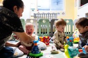 A teacher comforts a young child at a daycare as other toddlers play.