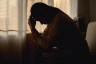 Silhouetted woman sits with her head in her hands in a dimly lit room.