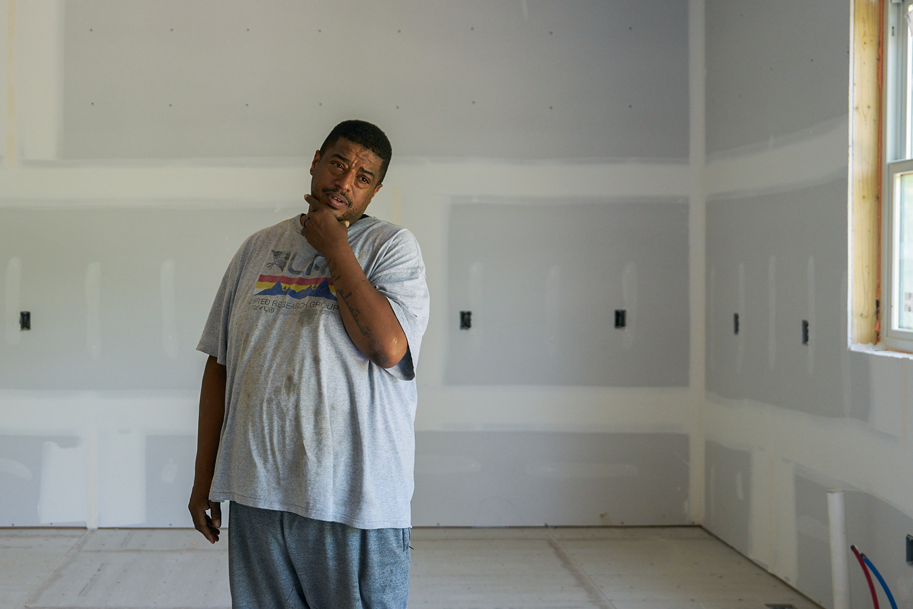 Isa Conway stands alone inside a bare room with unfinished drywall and no flooring.