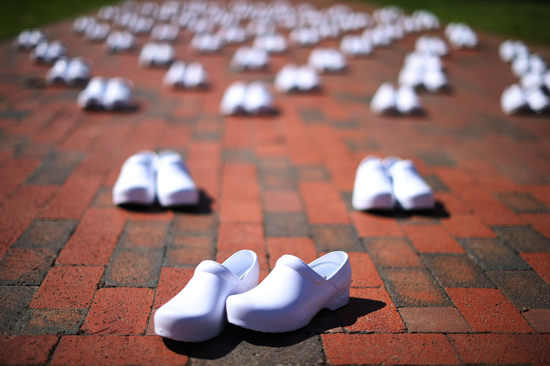 Rows of empty white nurse shoes lined up on a brick path, representing nurses who died from COVID-19, part of a protest in Washington, D.C.