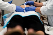Doctors measure the belly of a pregnant person who lays on a table.