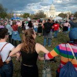 A crowd of demonstrators, many wearing or carrying Pride flags and gear, join hands in a line facing the Capitol during a rally in Washington, D.C.