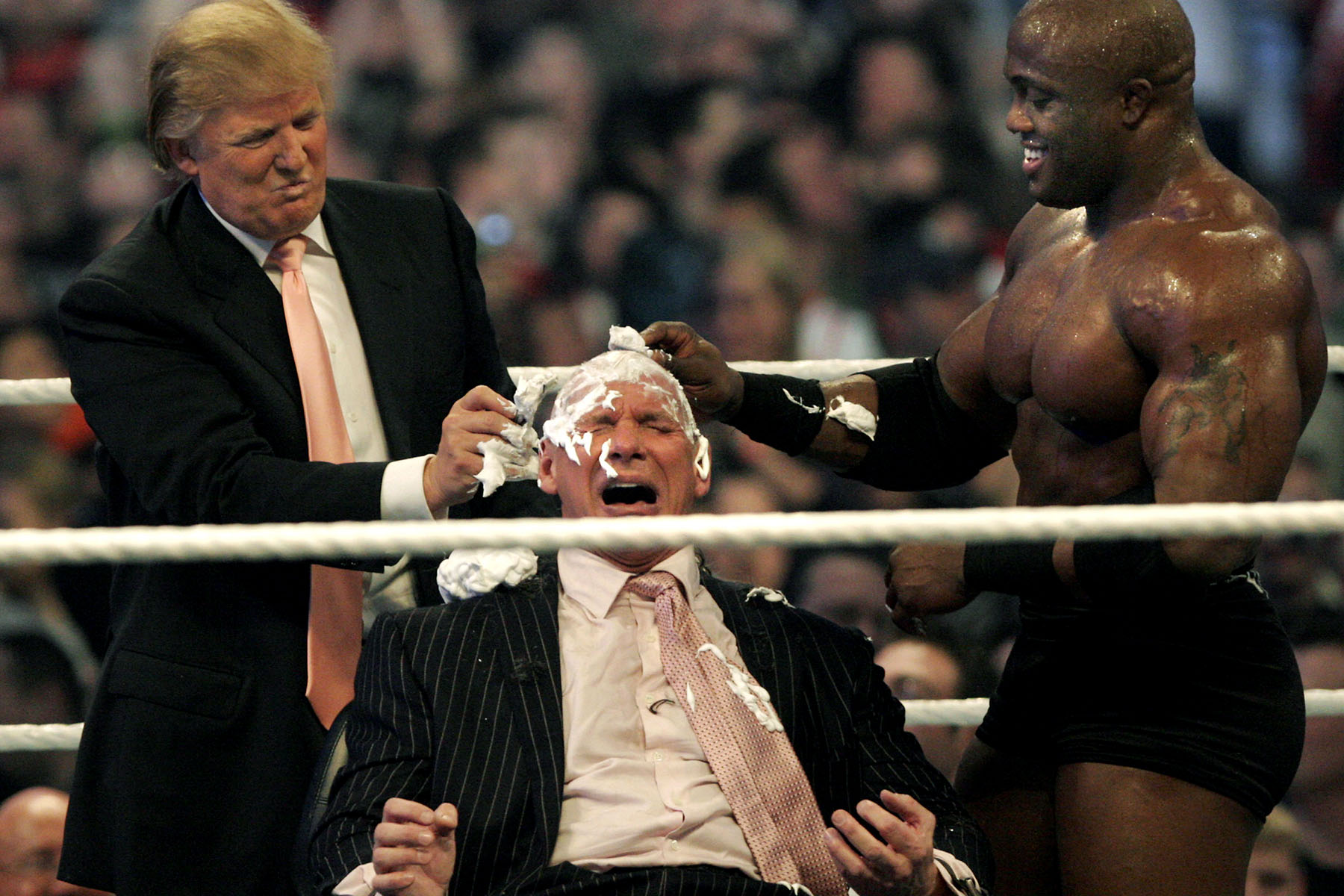 Donald Trump and wrestler Bobby Lashley shave Vince McMahon’s head in a wrestling ring as part of a WrestleMania stunt, with McMahon wincing dramatically.