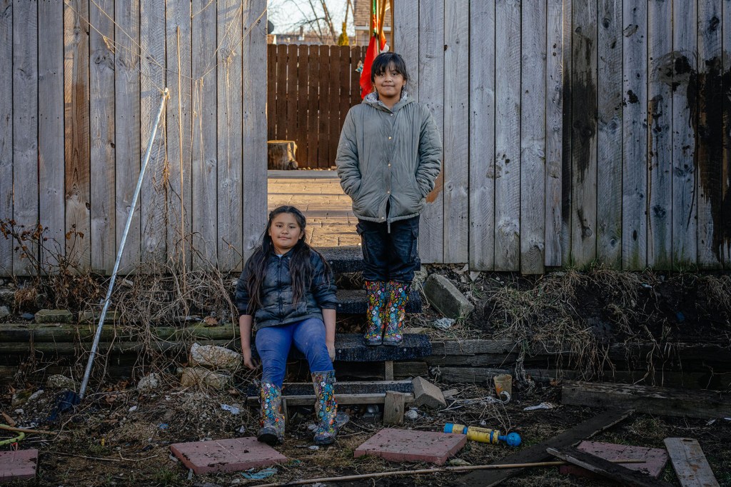 Elizabeth and Paola pose outside near their backyard fence in rubber boots.