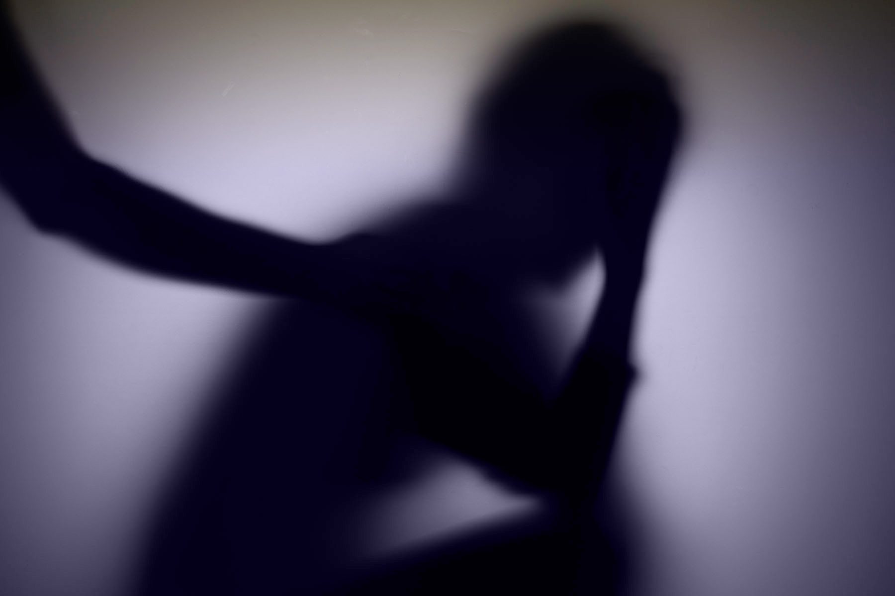 A blurred, shadowy silhouette of a person holding their head in one hand.
