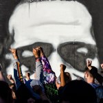 Protestors raise their fists in the air against the backdrop of a George Floyd mural.