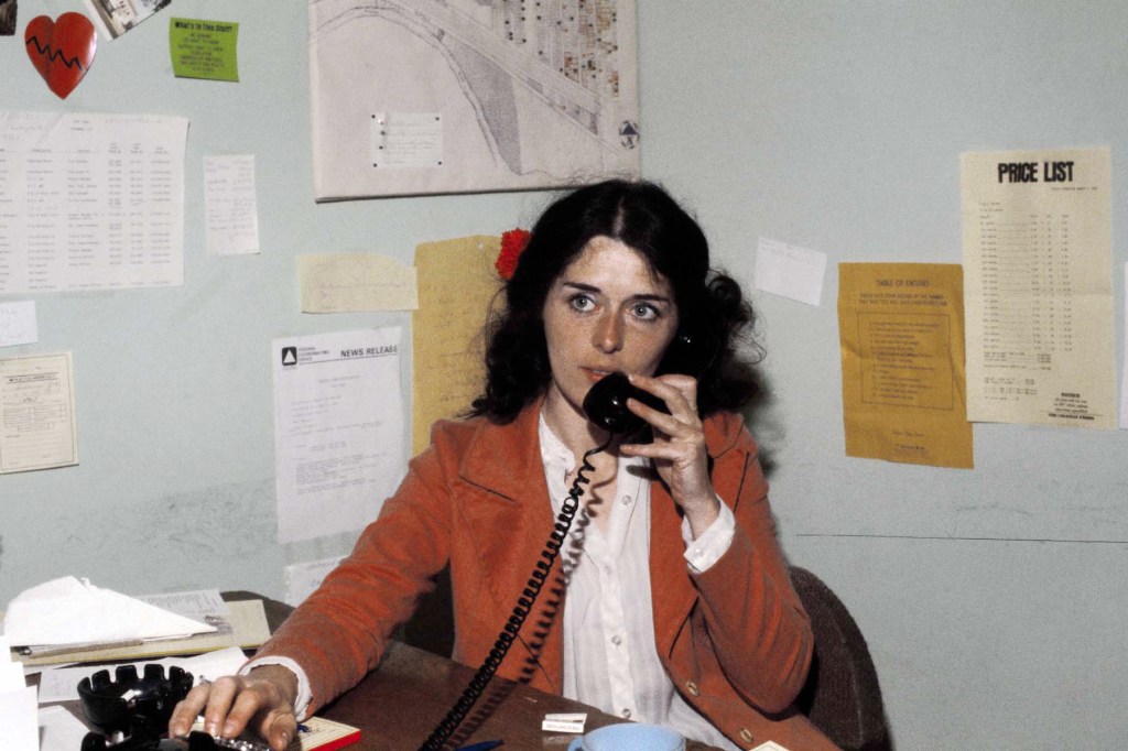 Lois Gibbs, president of the Love Canal Homeowners Association, speaks on the phone at a desk covered in papers and maps.