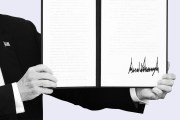 A close-up of President Trump holding open a signed executive order with a large signature visible on the right page.