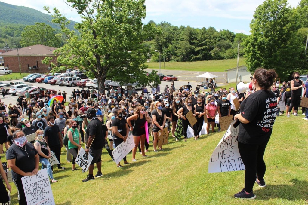 A group of protestors stand on a hill listening to a person with a bullhorn.