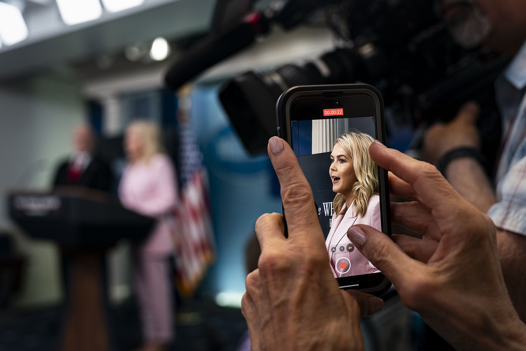 A person records White House Press Secretary Karoline Leavitt on their phone as she speaks at a press briefing.