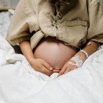 A pregnant person sits in a hospital bed wearing a hospital gown.