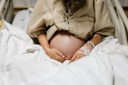 A pregnant person sits in a hospital bed wearing a hospital gown.