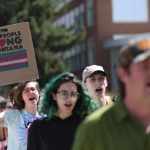 Transgender rights activists i march through the University of Montana campus on May 03, 2023 in Missoula. One holds a sign saying, 