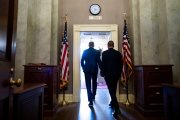Two politicians walk through a door, seen from behind with a clock above the door.