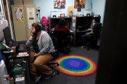 A person sits at a desk on the phone in an office with others on phones and a rainbow rug on the floor.