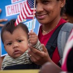 A woman holds a baby who holds an American flag.