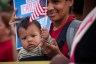 A woman holds a baby who holds an American flag.