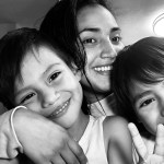 A woman smiles while she hugs her two sons close to her.