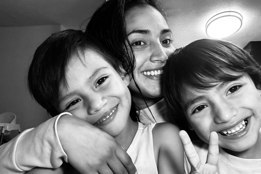 A woman smiles while she hugs her two sons close to her.