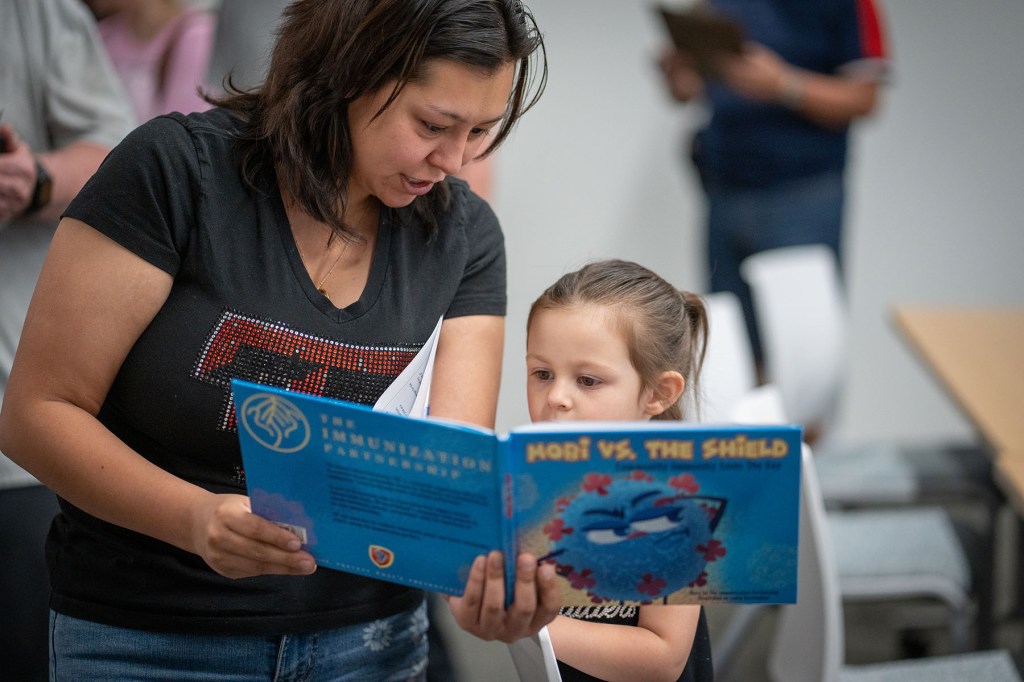A mother and daughter read a book about immunizations at a vaccine clinic.