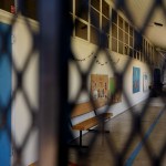 An empty school hallway is seen through a fence.