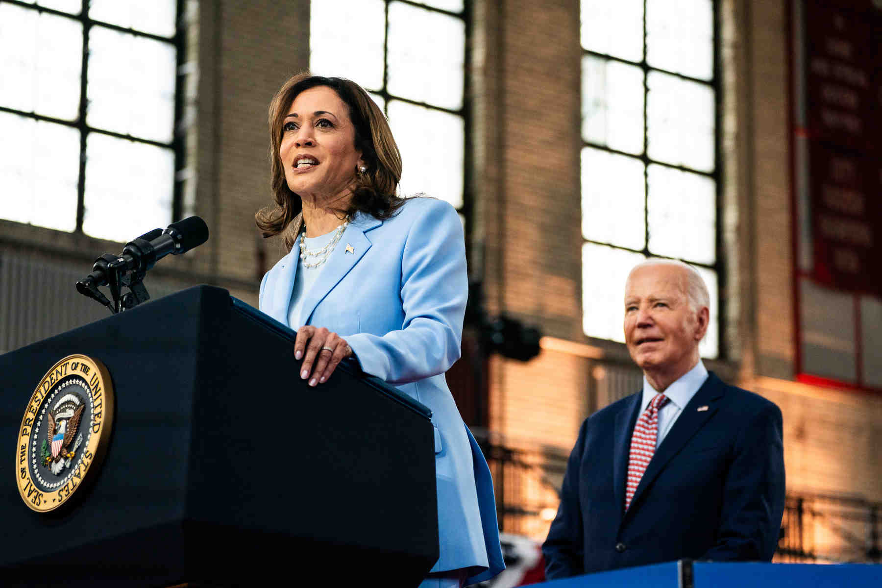 Kamala Harris stands at a podium with Biden standing behind her.