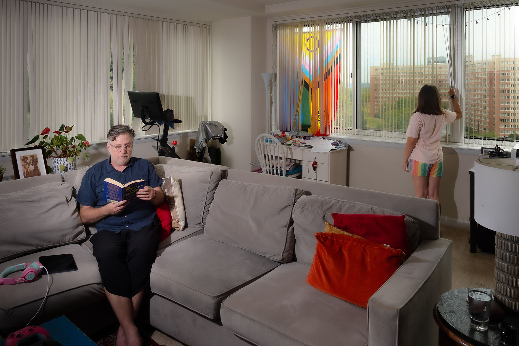 Brian reads on a couch as his daughter looks out the window behind him in their living room.