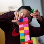 A child makes a tower with colorful Lego blocks.