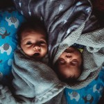 two twin baby boys are held at home in window light.