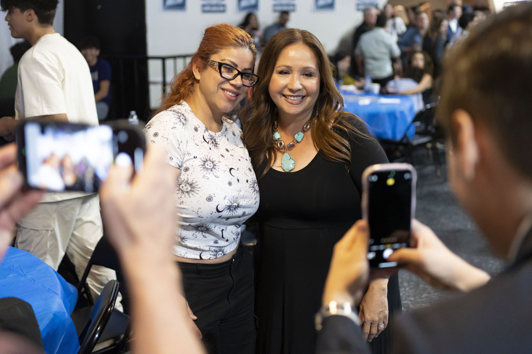Two women smile for photos being taken by two cell phones.