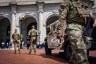 A National Guard walks while holding zip ties past a military vehicle as pedestrians are in the background.