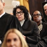 Several judges stand in a row listening to an unseen speaker.