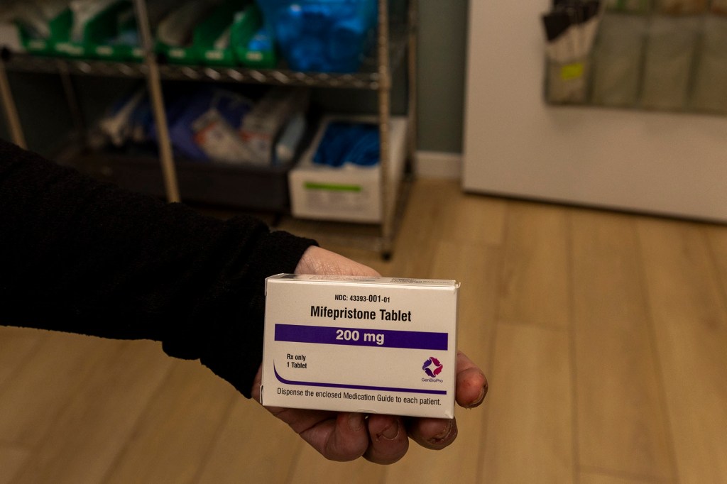A person holds a packet of Mifepristone inside a clinic.