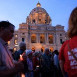 Unidentifiable people walk by a cathedral holding candles.
