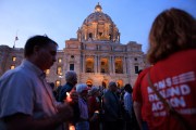 Unidentifiable people walk by a cathedral holding candles.