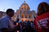 Unidentifiable people walk by a cathedral holding candles.