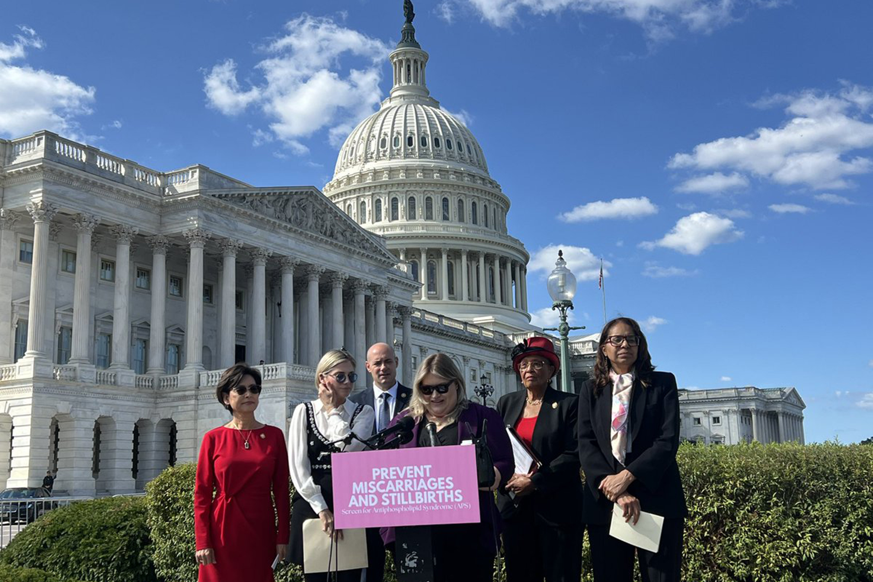 A group of lawmakers stand at a podium in front of the U.S. Capitol.