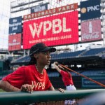 Baseball players stretch on the field with a WPBL billboard in the background.