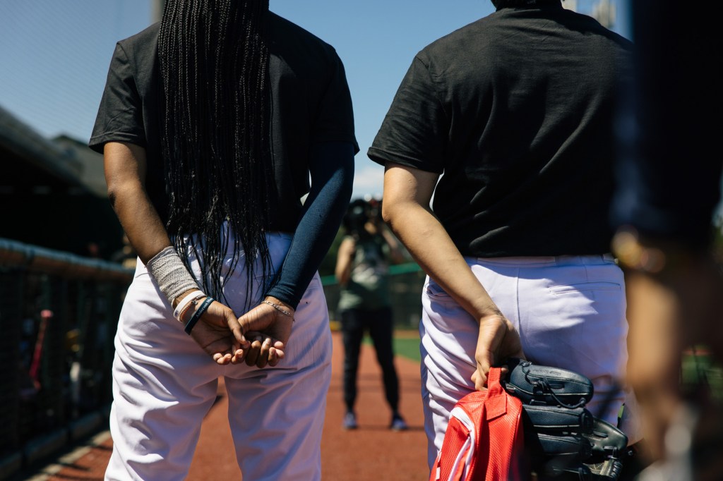Two players seen from behind, one holding a baseball glove.