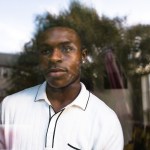 Amir looks out a window as he poses for a portrait at his home.