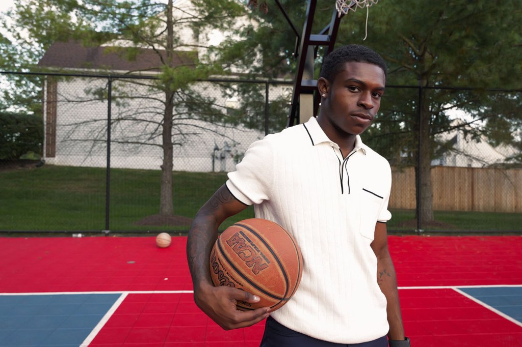 Amir poses for a portrait while holding a basketball on a court.